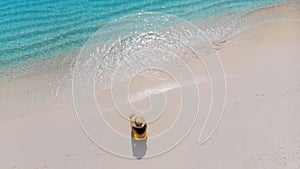 Girl alone on seashore and enjoys the sun. Young woman in a straw hat and yellow swimsuit.