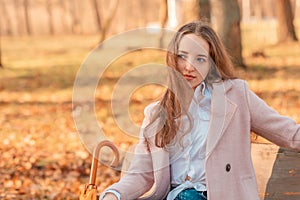 Girl alone sits with an umbrella in her hands on a bench in an autumn park