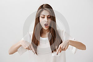 Girl is amazed standing on transparent floor. Portrait of overwhelmed attractive woman pointing down with index fingers