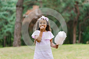 Girl in an amusement park in the summer eats cotton candy and smiles happily. The concept of summer holidays and school holidays