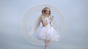 Girl angel with halo in white angel dress. A beautiful teen with blonde curly hair as cupid - Valentines Day. Love card