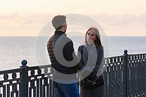 Girl anxiously looks at a guy near a railing in the background of the sea in cloudy weather