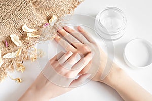 Girl applies moisturizer to her hands on a white background with dry flower petals and burlap. Ecological  natural fragrance-free