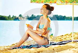 Girl applying sun tan cream on her skin on the beach