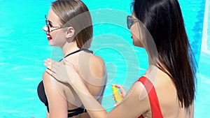 Girl applying sunscreen lotion to female friends back, skin care on vacation