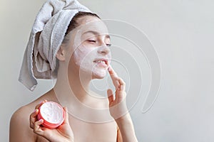 Girl applying white facial mask isolated on white background. Young woman in towel on head with white nourishing mask or
