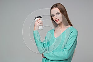 Girl in aquamarine jamper drinks coffee from paper plastic glass