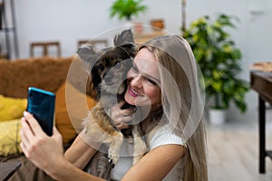 Girl in arms holds dog and they take selfie together. Multi-breed dog.