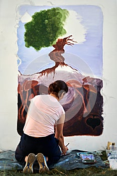 Girl artist draws with paint brush surreal nature landscape on white canvas rear view