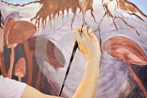 Girl artist hand holds paint brush and draws abstract surreal landscape on canvas