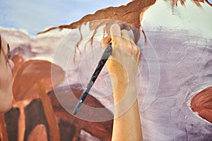 Girl artist hand holds paint brush and draws abstract surreal landscape on canvas