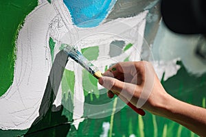 Girl artist hand holds paint brush and draws green nature landscape on canvas