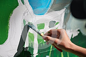 Girl artist hand holds paint brush and draws green nature landscape on canvas