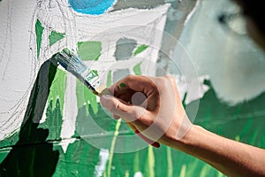 Girl artist hand holds paint brush and draws green nature landscape on canvas