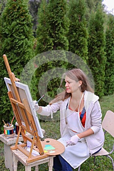 Girl artist paints picture and sits on chair at easel sides of t