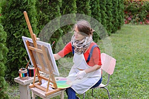 Girl artist paints picture and sits on chair at easel sides of t