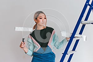 A girl of Asian appearance makes home repairs. Young woman paints the wall white