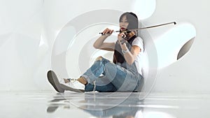 Girl of asian appearance sitting on the floor playing a violin