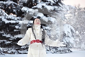 A girl of Asian appearance throws snow in a clearing in the snow