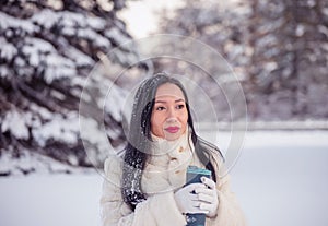 A girl of Asian appearance walks with a thermo mug with tea in her hands