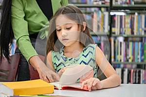 Girl ask for teacher to answer question in book while reading book at school library. Education and learning concept
