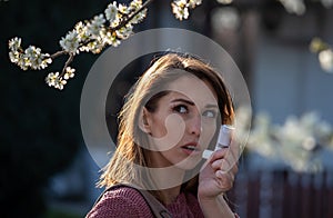 Girl with asthma pump in front of blooming tree in spring
