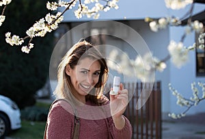 Girl with asthma pump in front of blooming tree in spring