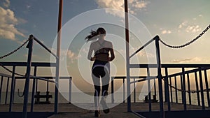 Girl athlete with a beautiful figure runs on the pier of the sea. sportswoman finishes the workout and happily raises