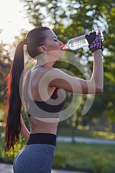 Girl athlete with a bottle in his hands drinks water while exercising in the park