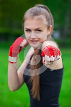 The girl the athlete, the boxer, in the park also gives the hand compressed in a fist forward with the reeled sports, red bandage.