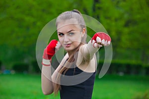 The girl the athlete, the boxer, in the park also gives the hand compressed in a fist forward with the reeled sports, red bandage.