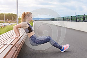 Girl athlete doing push-UPS from the bench on the waterfront.