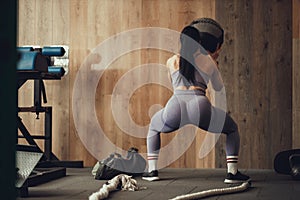 A girl athlete with a pumped-up booty squats with a phyto ball near the wall