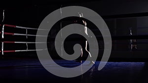 Girl athlete trains in the dark ring beats her legs . Silhouette. Slow motion