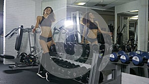 A girl of athletic build in a sports suit in a sports hall turns around near the mirror and shows a class, coach