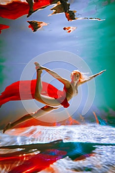 girl with an athletic figure, with red material and light underwear, in a ballet pose underwater