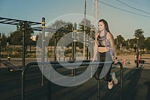 A girl of an athletic physique is engaged on the uneven bars on a street playground