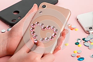 Girl attaching pink rhinestone heart onto beige phone case.