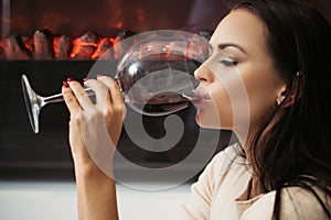 Girl attractive woman makeup face drinking wine wineglass background fireplace background. Luxury wine. Enjoy noble