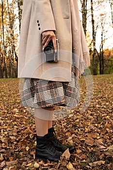 A girl in autumn clothes stands in the autumn forest and holds an old camera. Portrait without face