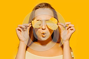 Girl with autumn leaves and red makeup, grimaces and has fun. Autumn photo on yellow background