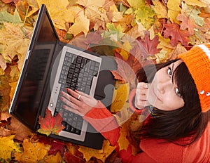 Girl in autumn orange foliage with laptop.