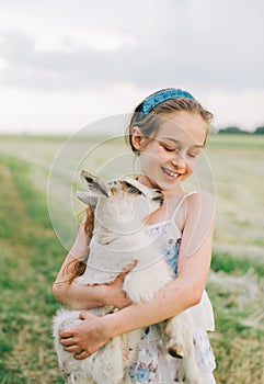 Girl with baby goat on farm outdoors. Love and care. Village animals. happy child hugs goat, concept of unity of nature