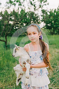 Girl with baby goat on farm outdoors. Love and care. Village animals. happy child hugs goat, concept of unity of nature