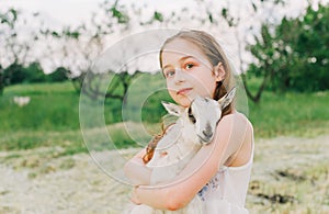 Girl with baby goat on farm outdoors. Love and care. Village animals. happy child hugs goat, concept of unity of nature