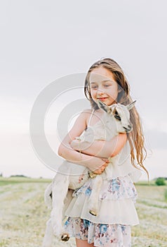 Girl with baby goat on farm outdoors. Love and care. Village animals. happy child hugs goat, concept of unity of nature