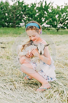 Girl with baby goat on farm outdoors. Love and care. Village animals. happy child hugs goat, concept of unity of nature