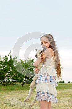Girl with baby goat on farm outdoors. Village animals. happy child hugs goat, concept of unity of nature and man