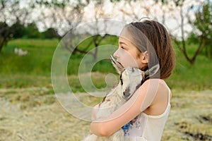 Girl with baby goat on farm outdoors. Village animals. happy child hugs goat, concept of unity of nature and man