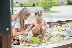 Girl and baby playing on sandbox. Toddler playing with sand molds and making mudpies